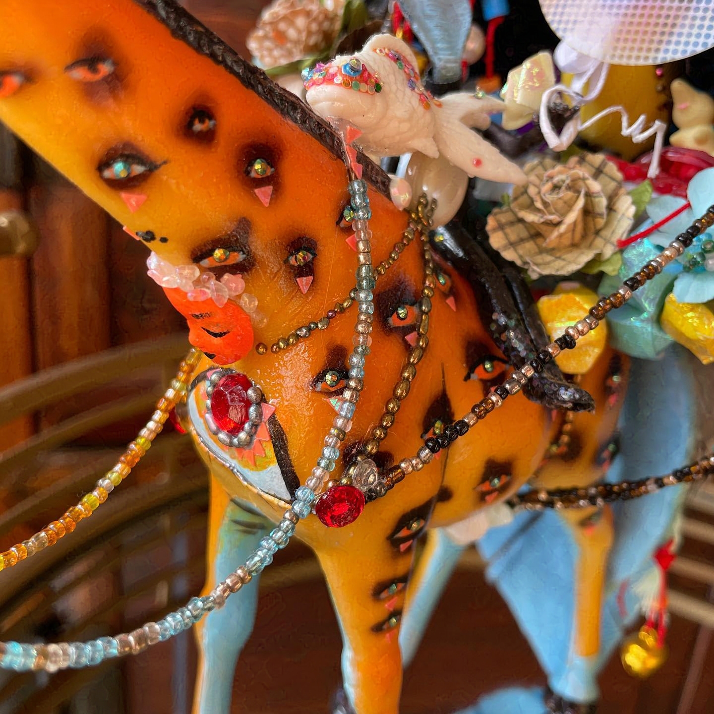 Giraffe spots have painted eyes, with rhinestone pupils. Doll face growing from the neck, and blue and orange beaded reins.