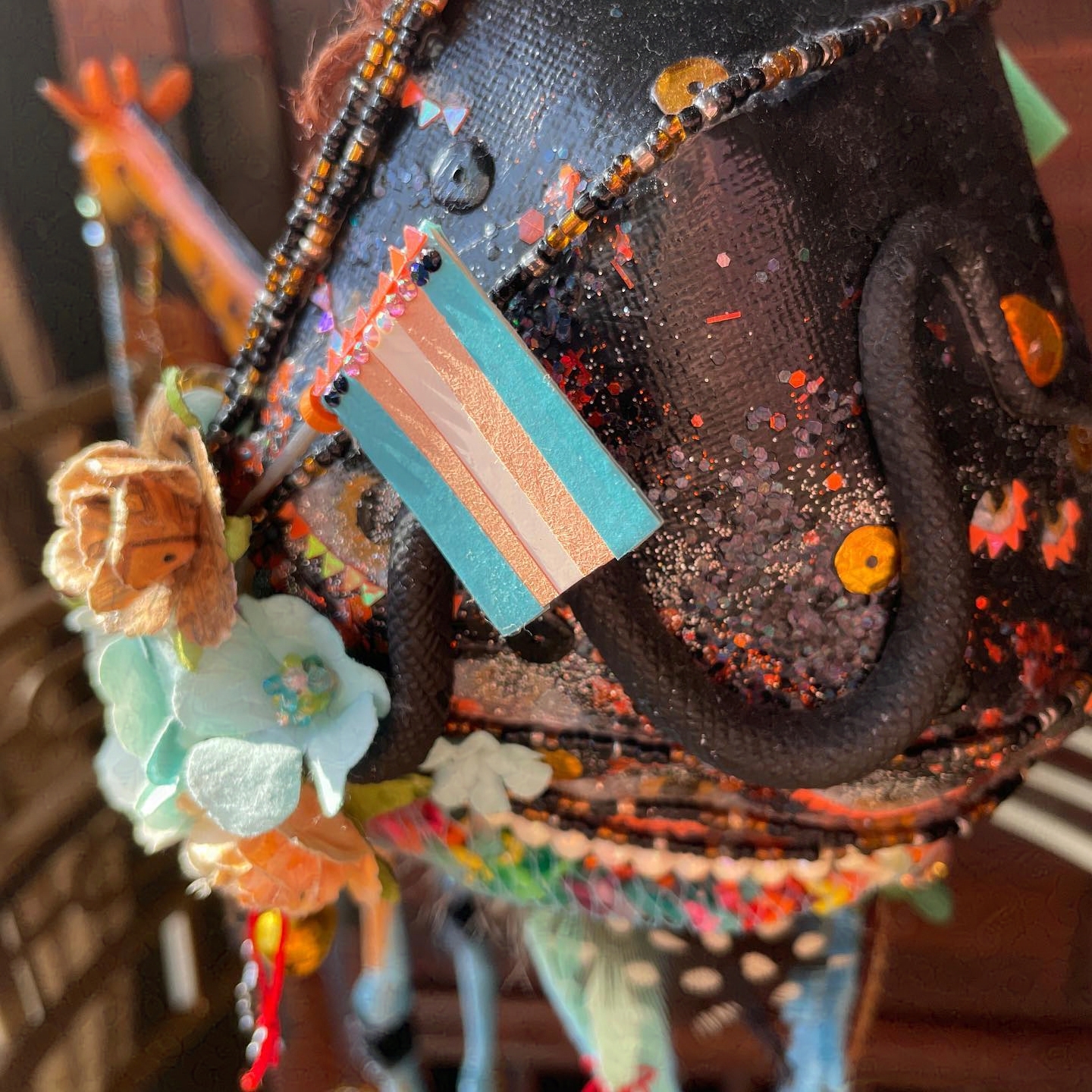 Trans flag on side of birdhouse. Other decorations include blue flowers, sequins, and a black snake.