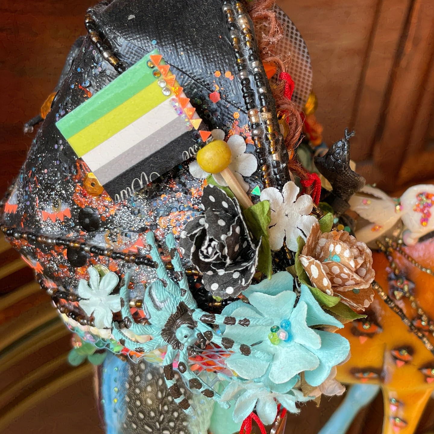 Aromantic flag on side of birdhouse. Other decorations include blue flowers, roses, and a spider.