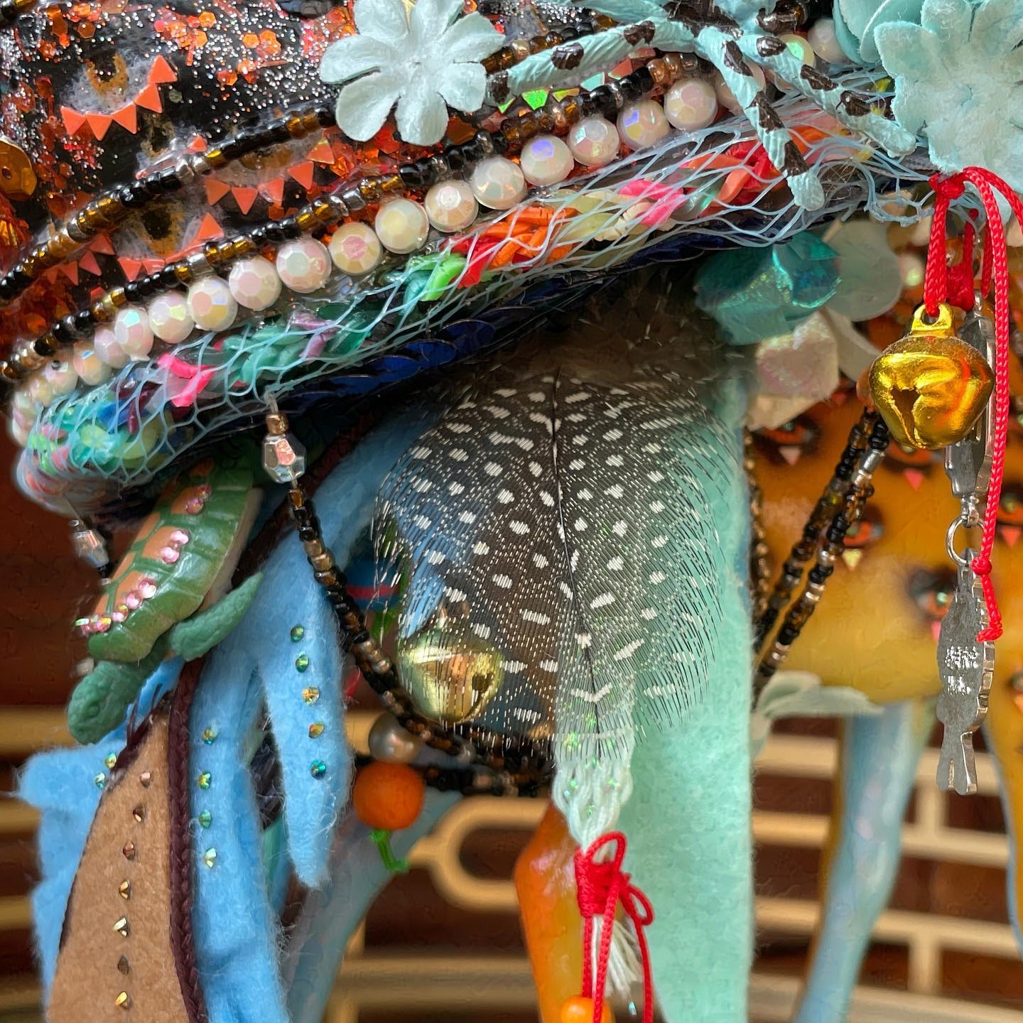 Trim of birdhouse has white sequins and blue netting covering a rainbow braided base. The giraffe's tail has feathers and bells attached.